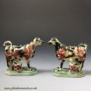 Pair of pottery cow creamers with milkmaids on green bases English circa 1815